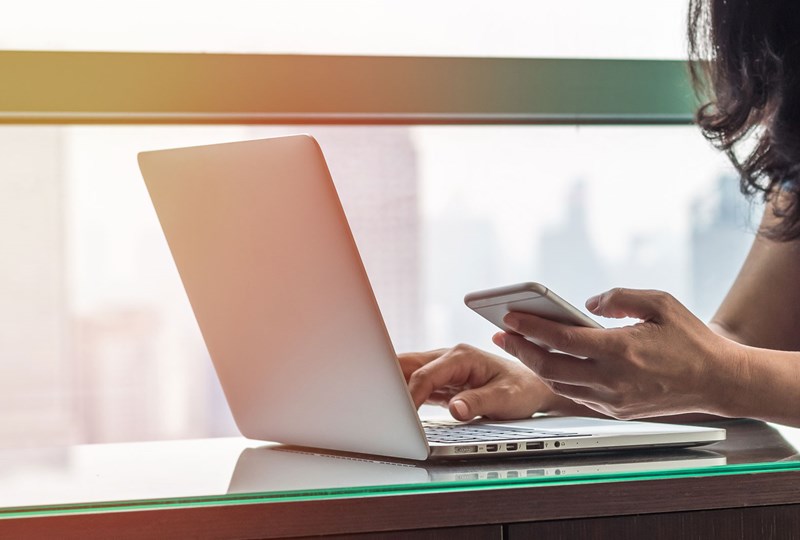 Woman working on a laptop and cell phone simultaneously