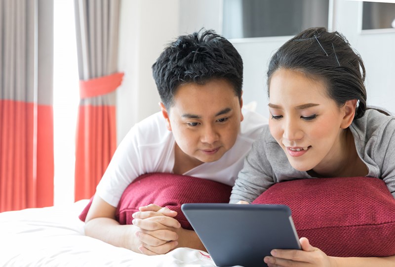 man and woman laying on a bed while browsing with their tablet